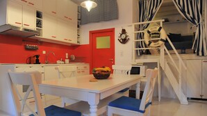 A kitchen with white cabinets, a red door, and a dining area with white and blue chairs. - Dandy Villas Velanidia Sailor's House - Private Maisonette - Sea View (Velanidia)