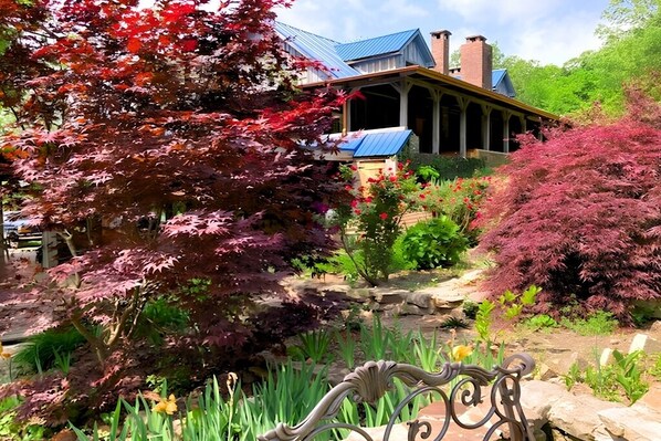 A house with a blue roof, a brick chimney, and a garden with various plants and a bench.