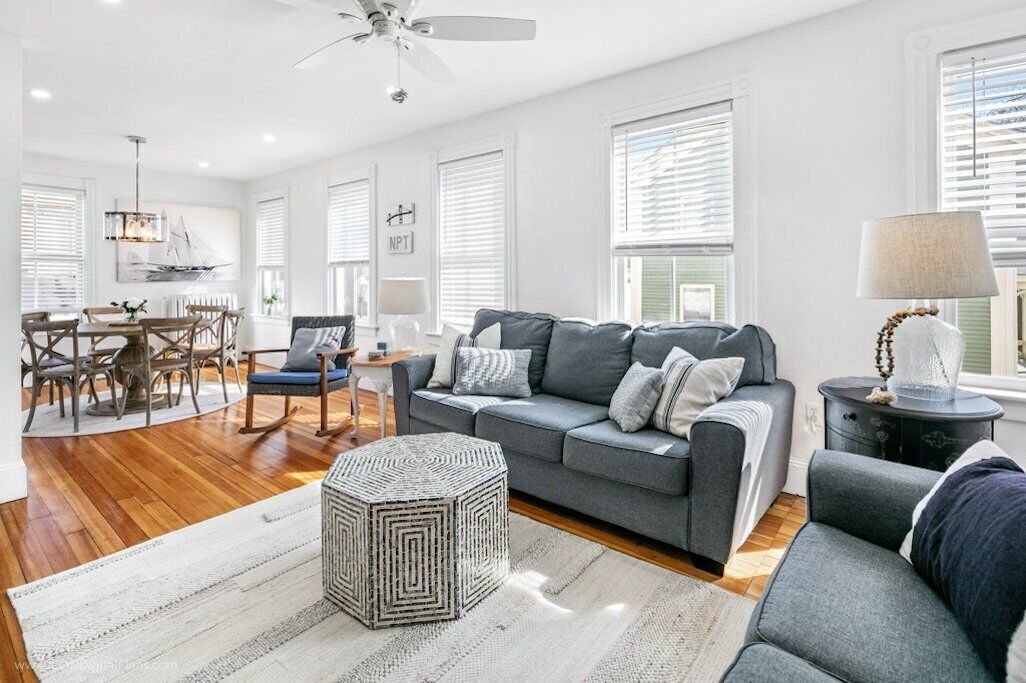 A spacious living room with a grey sofa, a round coffee table, and a dining area with a wooden table and chairs.