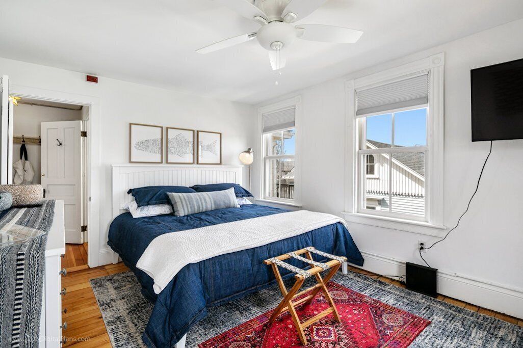A bedroom with a bed, a standing lamp, a TV, and a window with blinds.