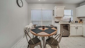 Une cuisine moderne avec des meubles blancs, une table de salle à manger ronde entourée de quatre chaises et une horloge au mur.