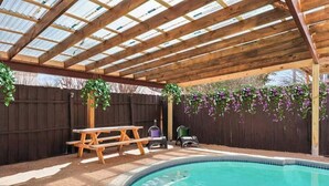 Une piscine extérieure couverte, dotée d’une terrasse en bois, d’une table de pique-nique et de chaises.