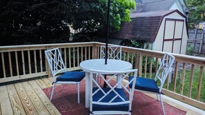 A wooden deck with a round table and chairs, a red patterned rug, and a white fence. - Spacious ranch 65” 4K tv deck, grill, fire pit fenced yd , office,  baby gear (Cape May Court House)