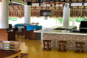 Uma área de bar com balcão de tijolos, mobiliário de vime e uma TV fixada na parede.
