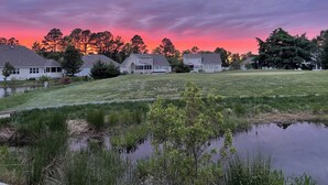 Un quartier résidentiel avec des maisons, un étang et des arbres, le tout baigné par la lumière d’un coucher de soleil.