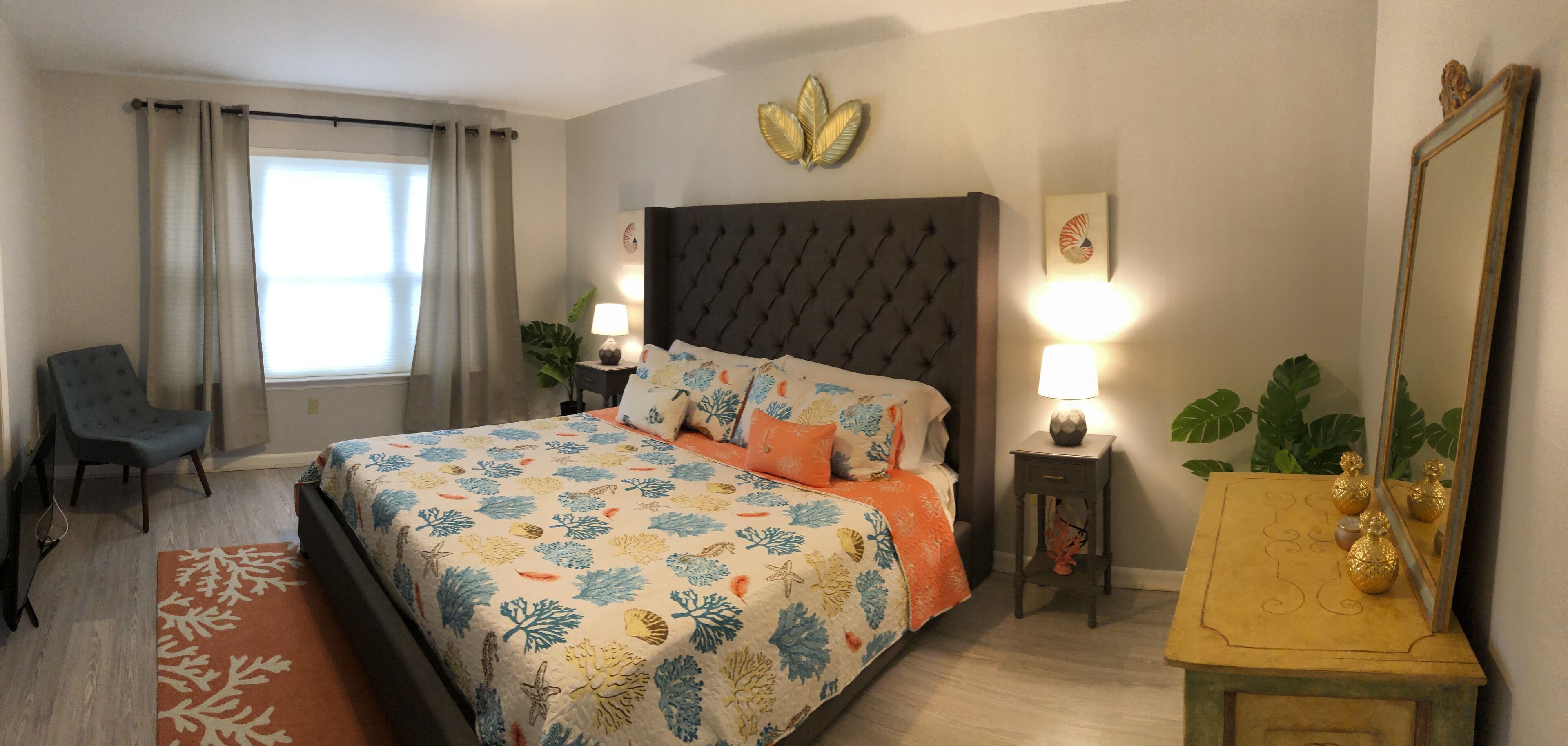 A bedroom with a bed, two bedside tables, a chair, a window with curtains, and wall decorations.