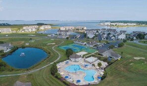 An aerial view of a residential area with multiple houses, a large swimming pool, and a lake.