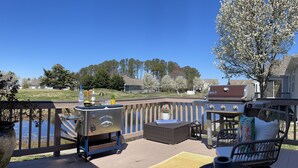 Une terrasse dotée de mobilier d’extérieur, d’un barbecue et offrant une vue sur un lac et des maisons en arrière-plan.
