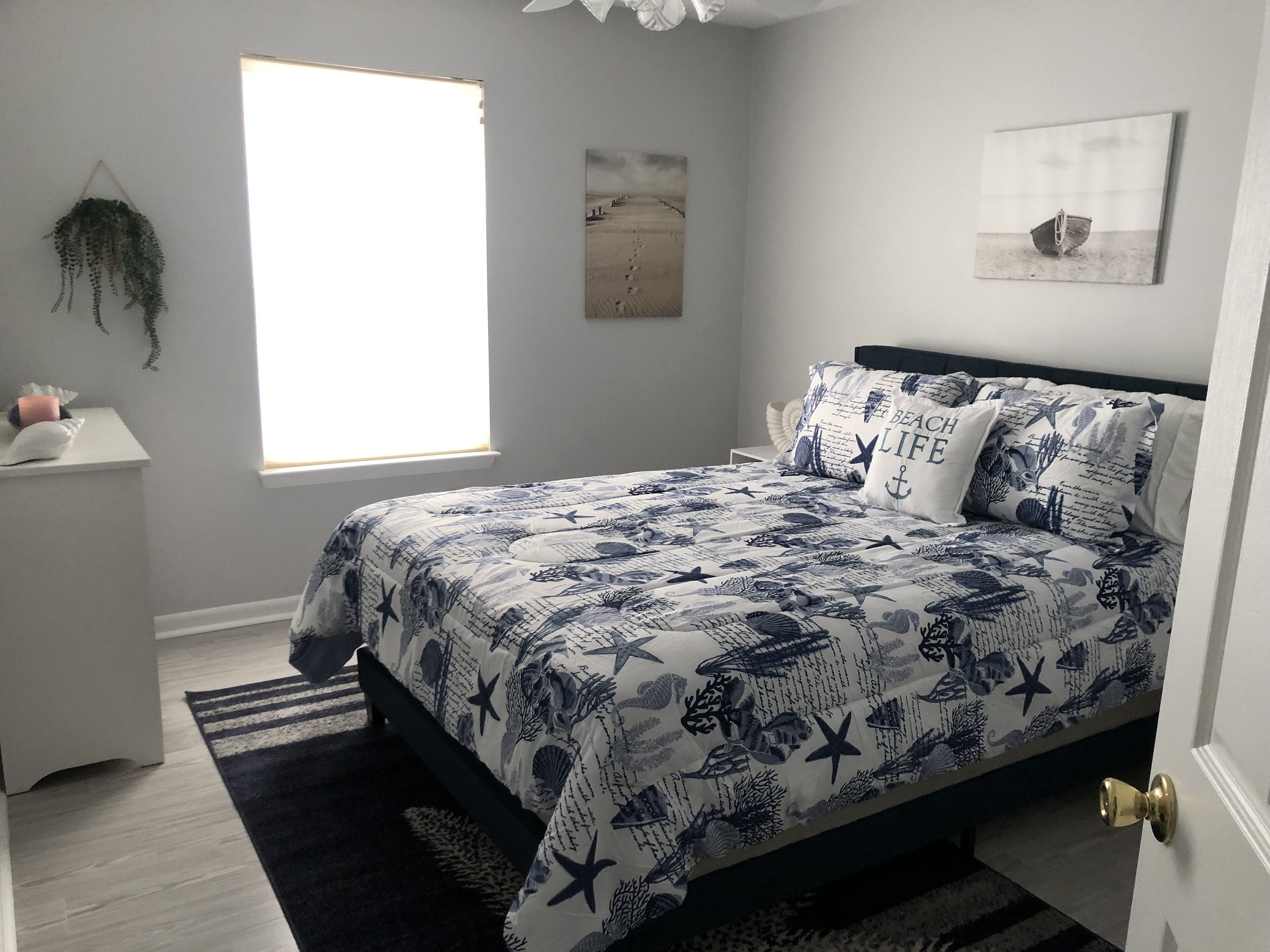 Un dormitorio con cama, mesita de noche, ventana y adornos en la pared.