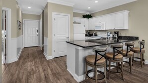 Una cocina con armarios blancos, encimera de granito negro y cuatro taburetes de madera.