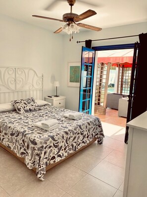 A bedroom with a bed, a nightstand, a ceiling fan, and a view of the outside. - Garden Villa (Playa Blanca)