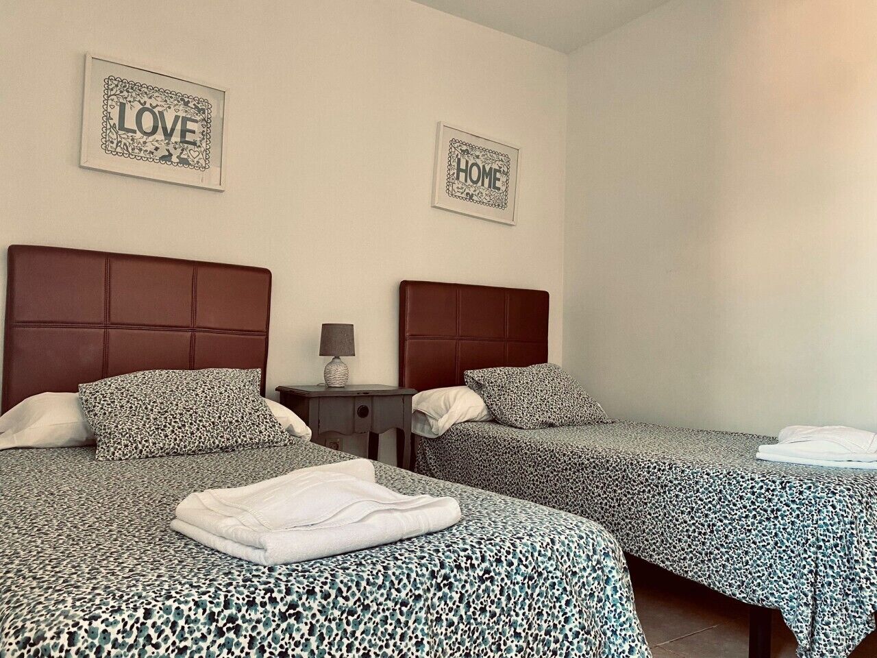 A hotel room with two beds, a nightstand, and two framed pictures on the wall.