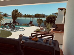 A patio with a pool, lounge chairs, a table with fruits and cups, and a view of a mountain. - Garden Villa (Playa Blanca)
