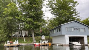 Una cabaña junto al lago con un muelle, un bote y un cobertizo pequeño.