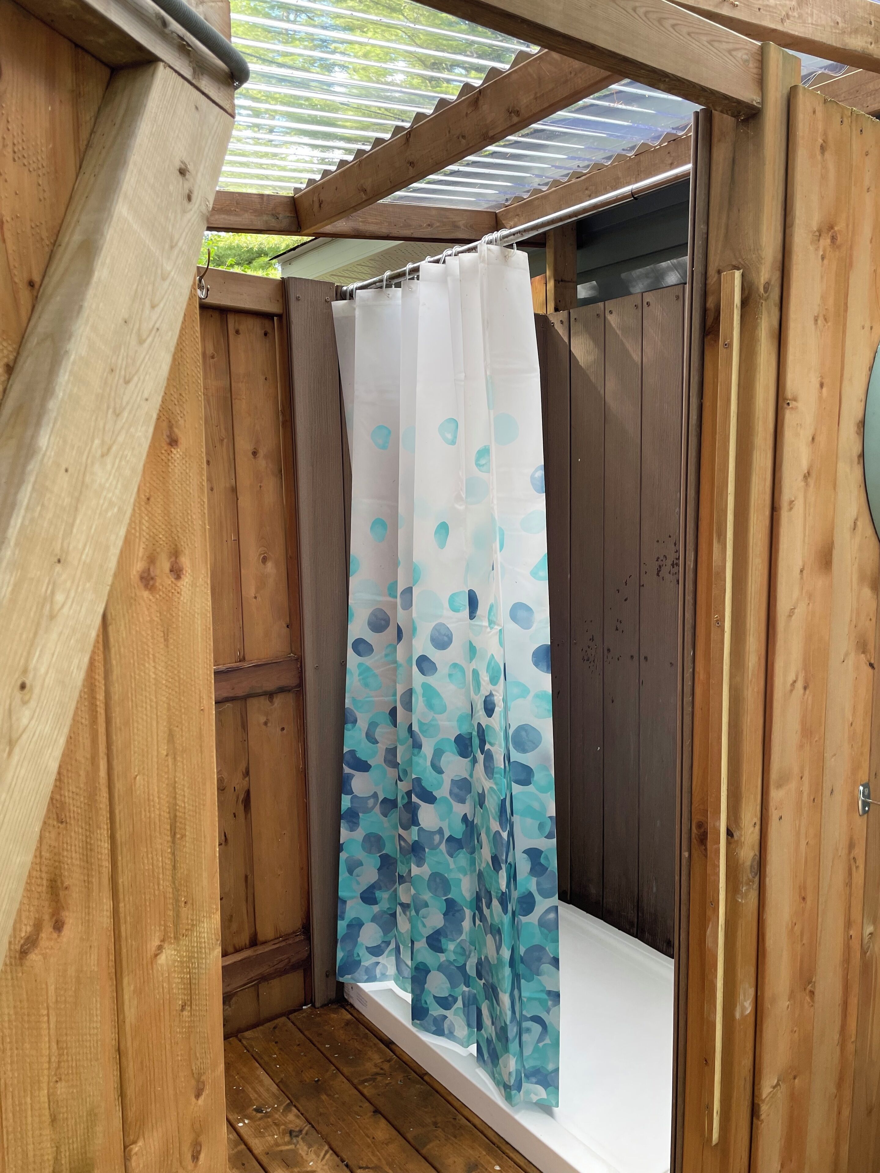 Un área de ducha exterior de madera con cortina blanca con motivos de hojas azules.