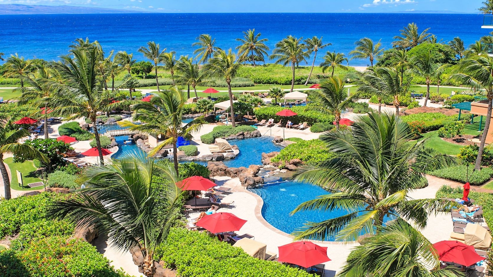 Ein Resort mit mehreren Schwimmbecken, Palmen und Blick auf den Ozean.