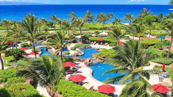 A resort with multiple swimming pools, palm trees, and a view of the ocean.