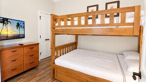 Un lit superposé avec une structure en bois, une commode avec des tiroirs et un téléviseur fixé au mur.