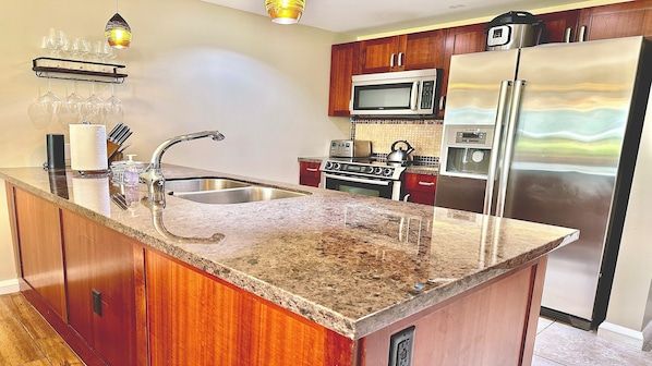Una cocina con encimeras de granito, electrodomésticos de acero inoxidable, armarios de madera y microondas integrado.