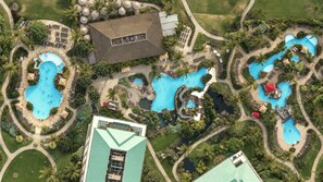 Une vue aérienne d’un complexe hôtelier doté de plusieurs piscines, d’un aménagement paysager luxuriant et d’un bâtiment imposant surmonté d’un toit végétalisé.