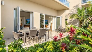 An outdoor patio with a dining table and chairs, surrounded by lush greenery and a view of the sea.