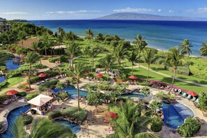 Un resort con varias piscinas, palmeras y vistas al océano.