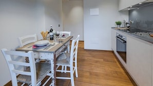 A modern kitchen with white cabinets, a wooden dining table, and a built-in oven.