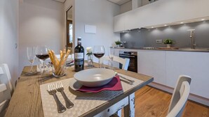 Ett modernt matområde med ett träbord dukat för två personer, med en vit tallrik, en rosa servett och en flaska vin.