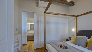 Une chambre à coucher avec un lit, une table de chevet et une commode. Il y a une chaise et un radiateur dans le coin.