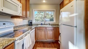 A kitchen with wooden cabinets, a white microwave, a stove, a refrigerator, and a window with a view of trees. - Scenic Escape - Best Views of Lake Tahoe! (Stateline)