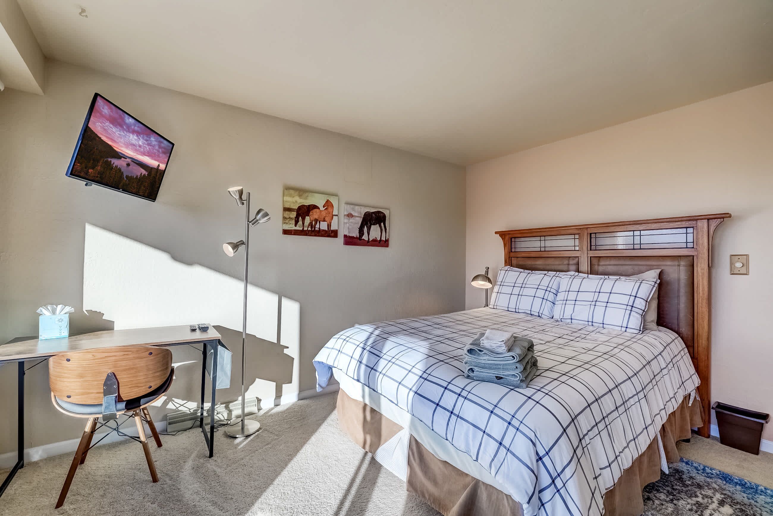 A bedroom with a bed, desk, chair, and artwork on the wall.