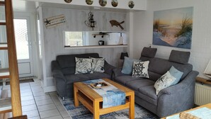Un salon chaleureux avec un canapé gris, une table basse en bois et un tableau représentant une scène de plage.