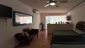 Een kamer met een bed, een bankje, een spiegel, een plafondventilator en een raam met gordijnen.