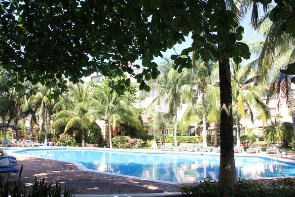 A swimming pool surrounded by palm trees and lounge chairs, with a building in the background.