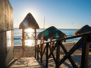 A wooden pier leading to a beach with thatched-roof structures.