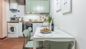 A kitchen with a washing machine, microwave, and a dining area with a table set for two. - Wine Apartments Florence Ciliegiolo  (Firenze)