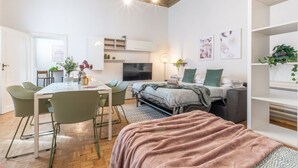 A modern, well-lit room with a dining table, chairs, a bed, and a TV.