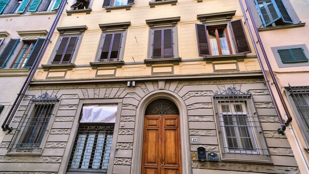 A building with a central wooden door, multiple windows with shutters, and a number '19' on the facade.