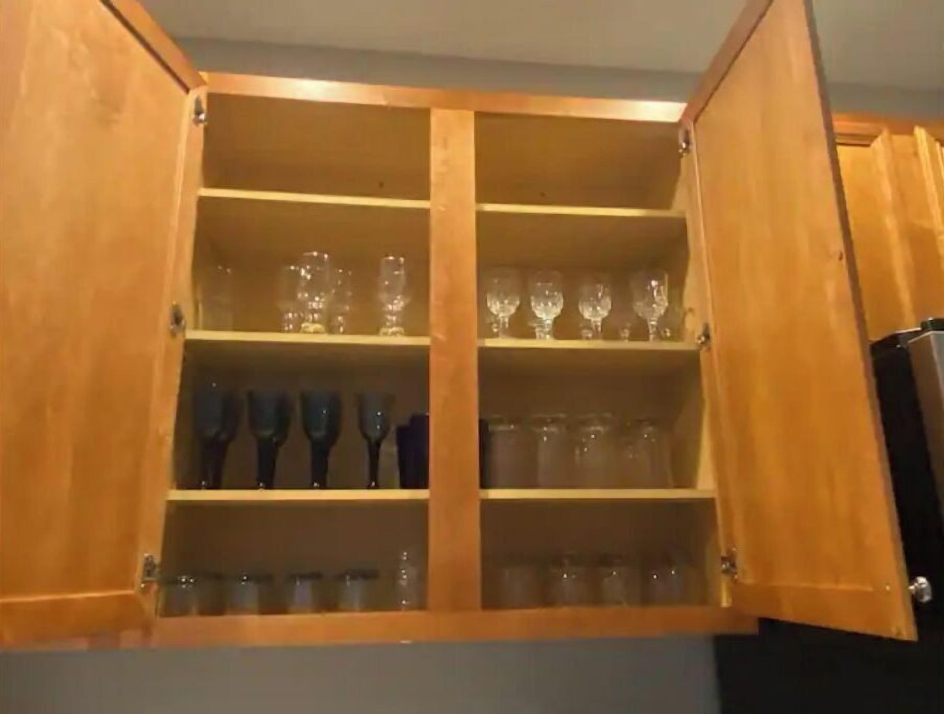A wooden cabinet with multiple shelves, some containing clear glassware and others with dark-colored items.