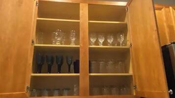 A wooden cabinet with multiple shelves, some containing clear glassware and others with dark-colored items.