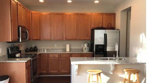 A modern kitchen with wooden cabinets, stainless steel appliances, and a large island with stools. - Breath and Relax/can sleep up to 6 guest/pets ok (Bluffton)