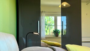 Un dormitorio con cama, lámpara de noche y vistas a un balcón con planta.