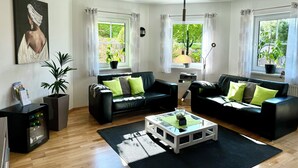 Una sala de estar con dos sofás negros, una mesa de centro de vidrio y una planta en maceta.