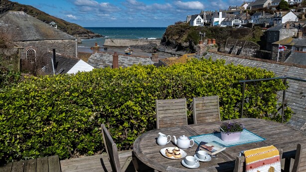 A wooden deck with a table set for tea, overlooking a coastal town with houses and cliffs.