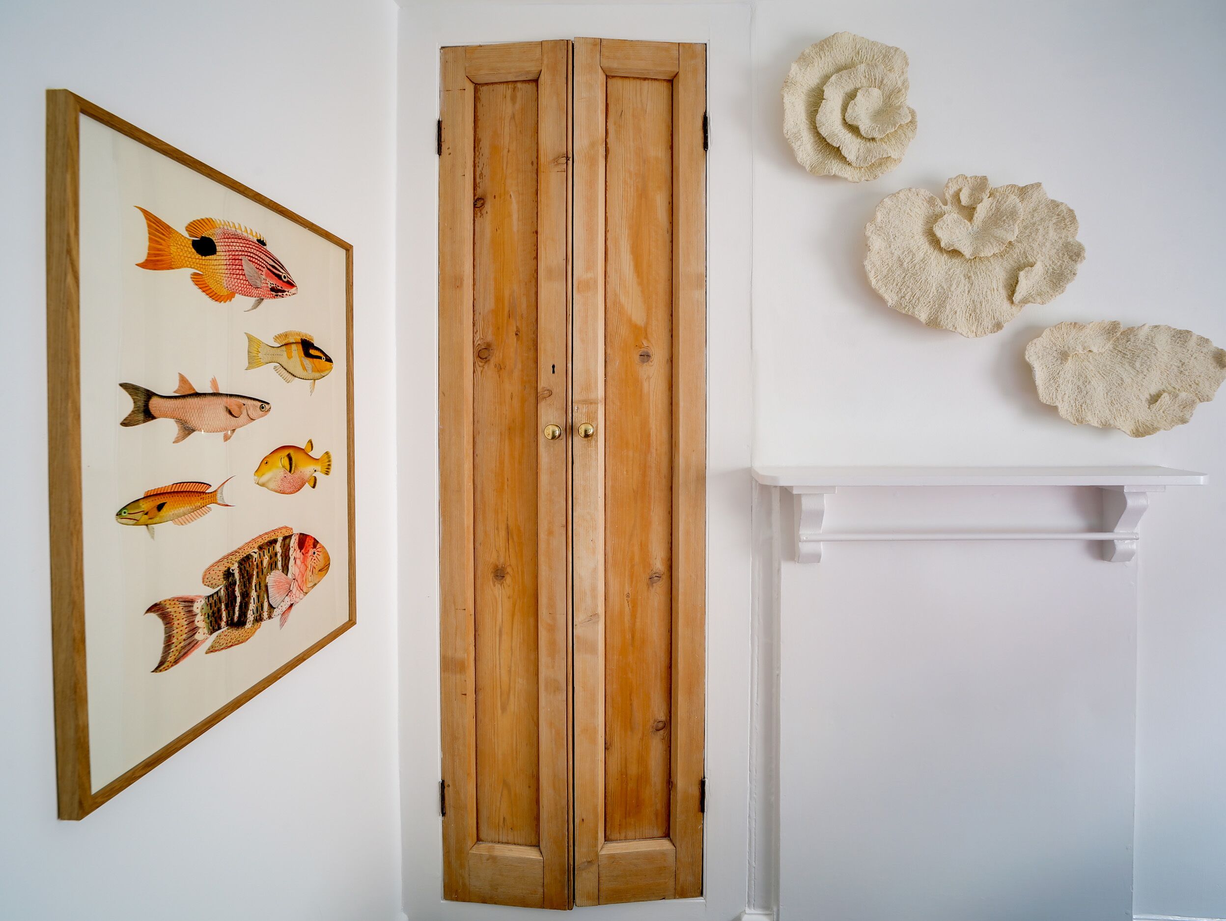 Ein Zimmer mit einem Holzschrank, einem Bild von Fischen in einem Rahmen und drei strukturierten Wanddekorationen.