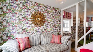 A living room with a striped sofa, a wooden coffee table with decorative items, and a wall with a fish and floral wallpaper.