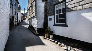 A narrow street with traditional stone and plaster buildings, a red telephone booth, and a sign for 'Grey Roofs'.