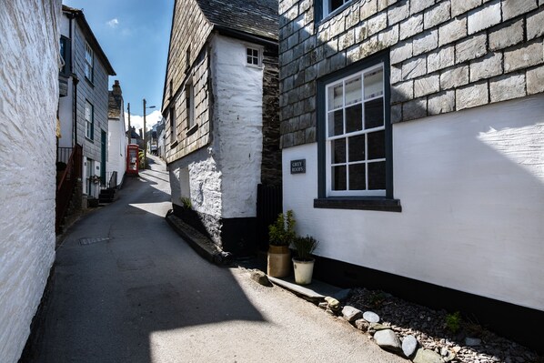 A narrow street with traditional stone and plaster buildings, a red telephone booth, and a sign for 'Grey Roofs'. - Grey Roofs (Port Isaac)