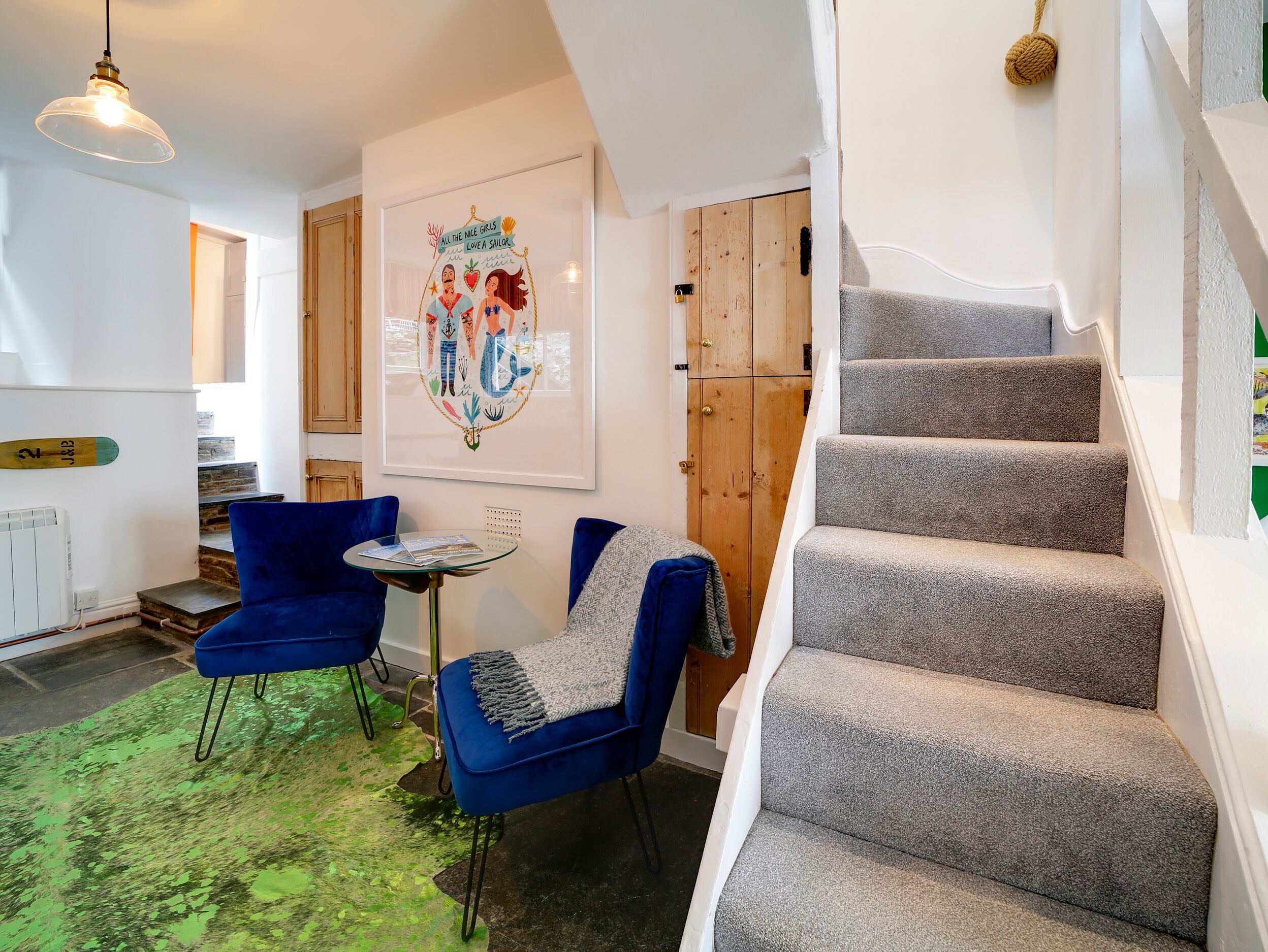 Ein modernes Interieur mit Treppe, blauen Stühlen, einer Holztür und einem gerahmten Kunstwerk.
