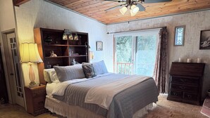 Un dormitorio con cama, cabecera de madera, mesita de noche con lámpara, estantería y cómoda.